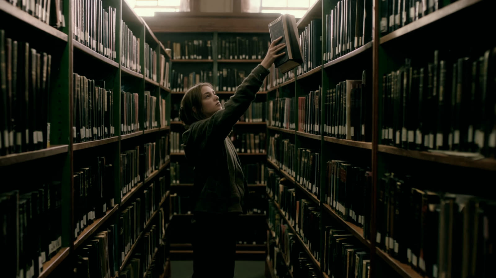 A person taking a bound journal from a high library shelf